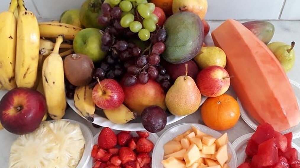 Mesa com frutas frescas de várias cores: banana, uva, maçã, pera, mamão, abacaxi e morango